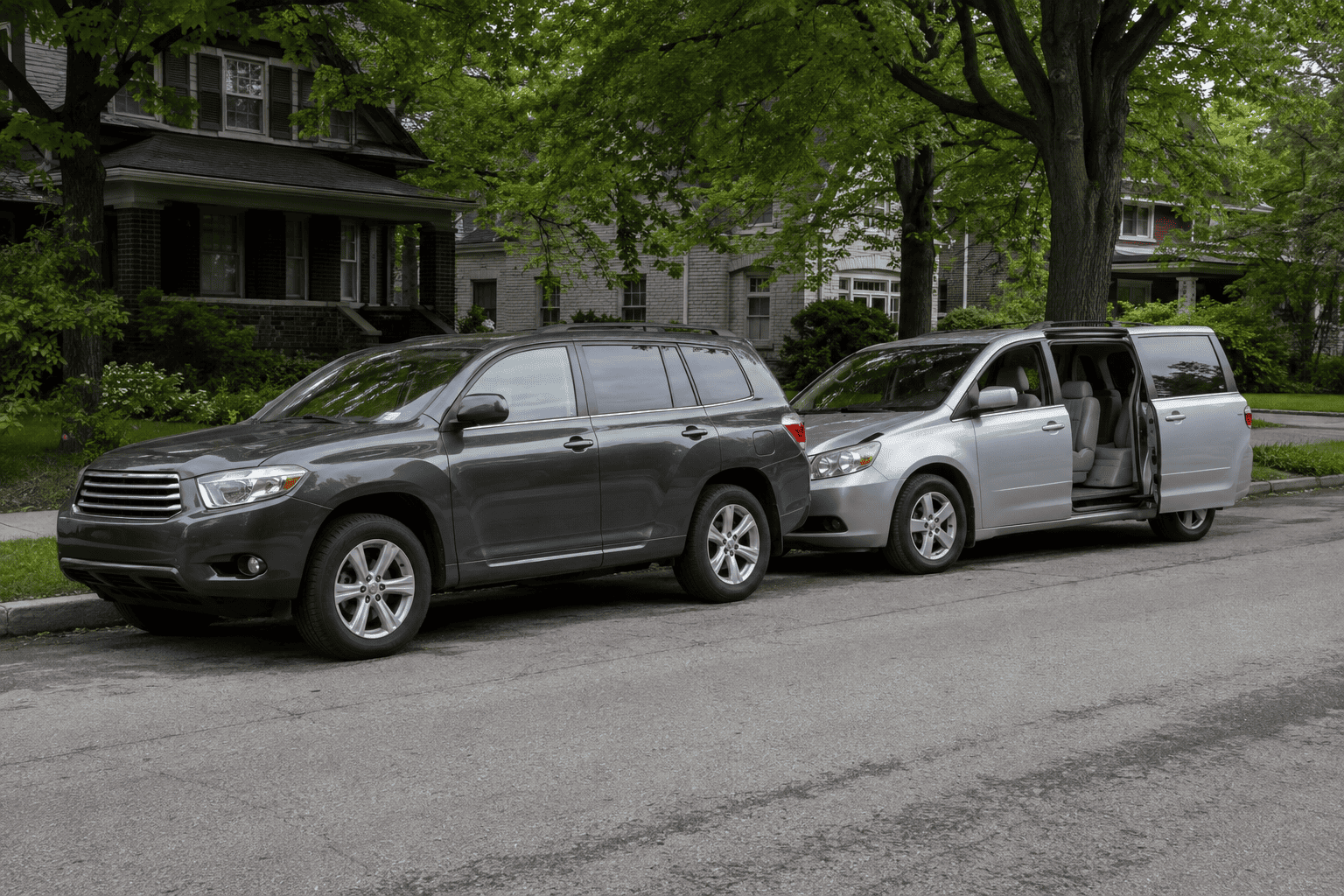 A used three-row SUV and a minivan with a sliding door open, parked on a residential street in Passaic Park, New Jersey